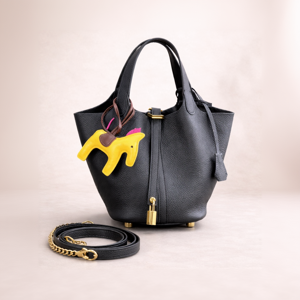 Black handbag with a yellow dog-shaped charm on a light beige background